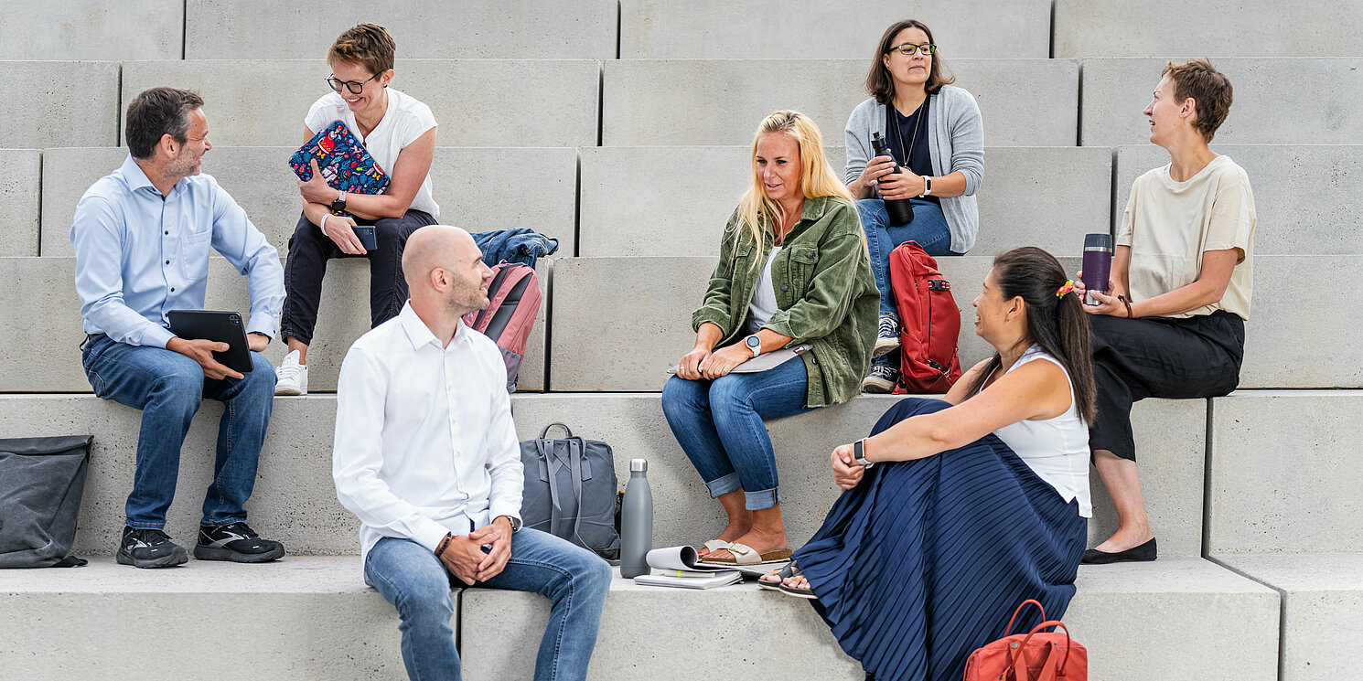 Mehrere Studierende sitzen mit ihren Lernmaterialien auf einer großen Treppe.