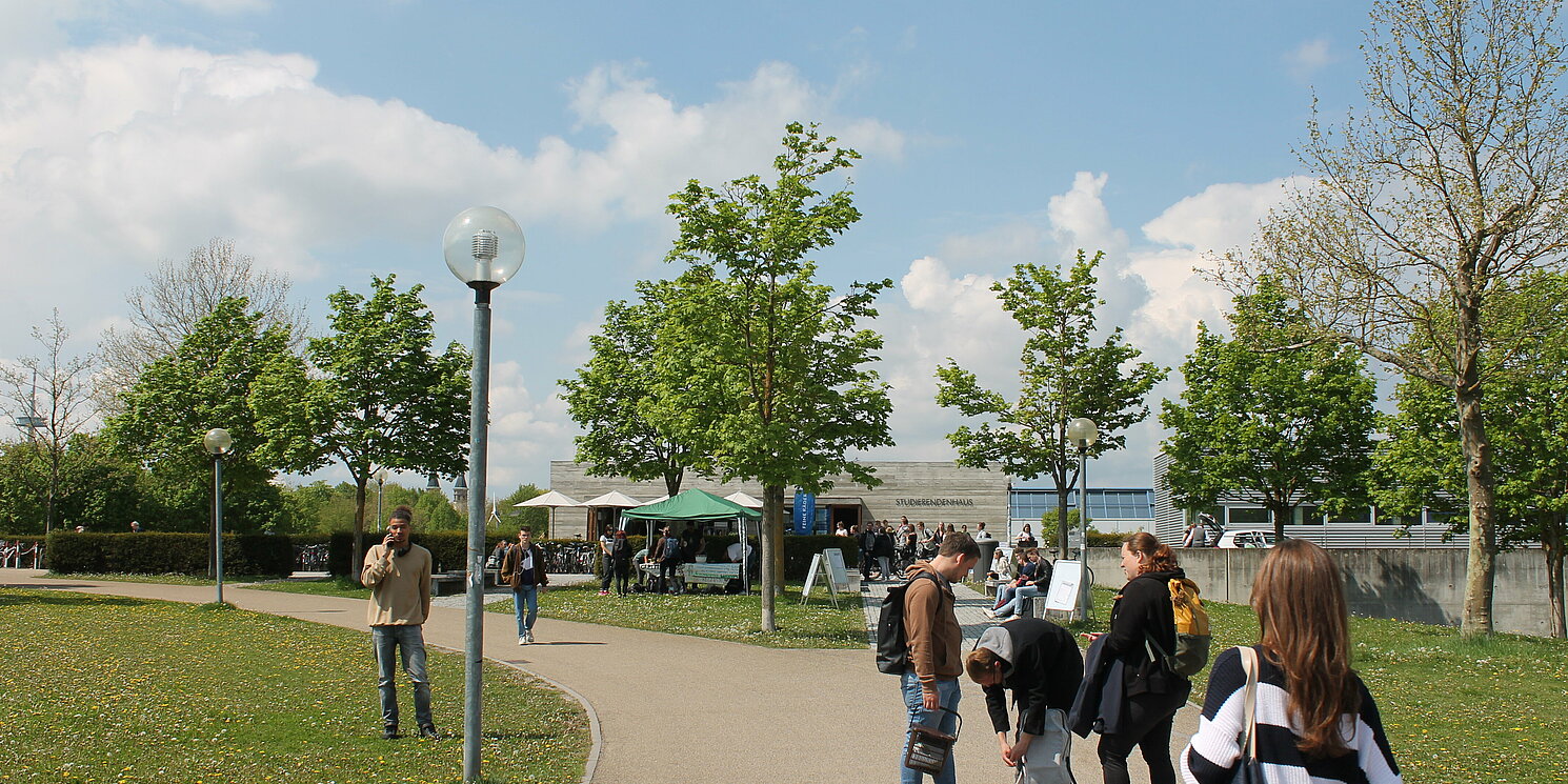 Auf dem Foto ist der Campus der OTH Regensburg im Sommer zu sehen. Im Hintergrund sieht man einen Stand mit Lebensmitteln von Foodsharing.