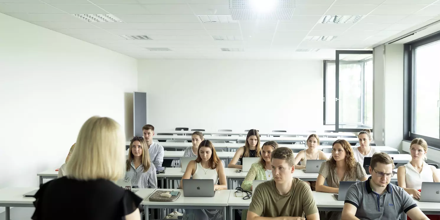 Eine Gruppe von 13 Personen sitzt in einem Hörsaal. Die Fenster sind geöffnet.