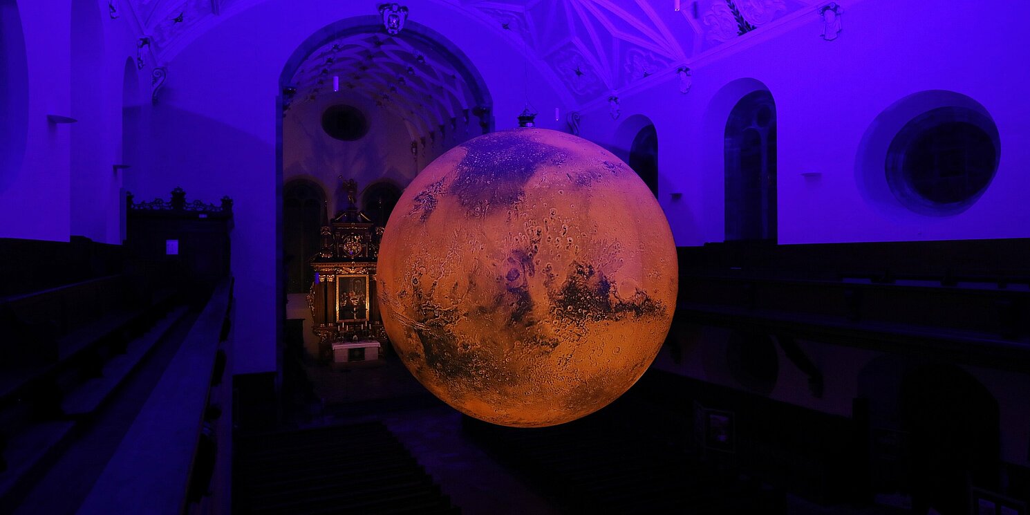 Über dem Mittelschiff der Dreieinigkeitskirche erstrahlt ein riesiges Mars-Modell. Foto: Stadt Regensburg/Stefan Effenhauser 