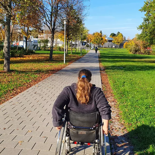 Eine Rollstuhlfahrerin fährt einen Weg entlang.