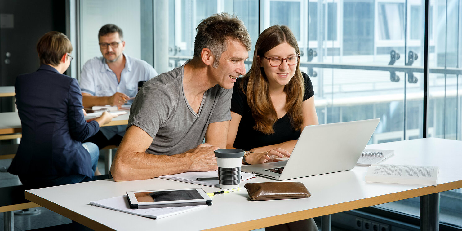 Vier Studierende lernen und arbeiten an ihren Tischen mit Büchern und Laptops