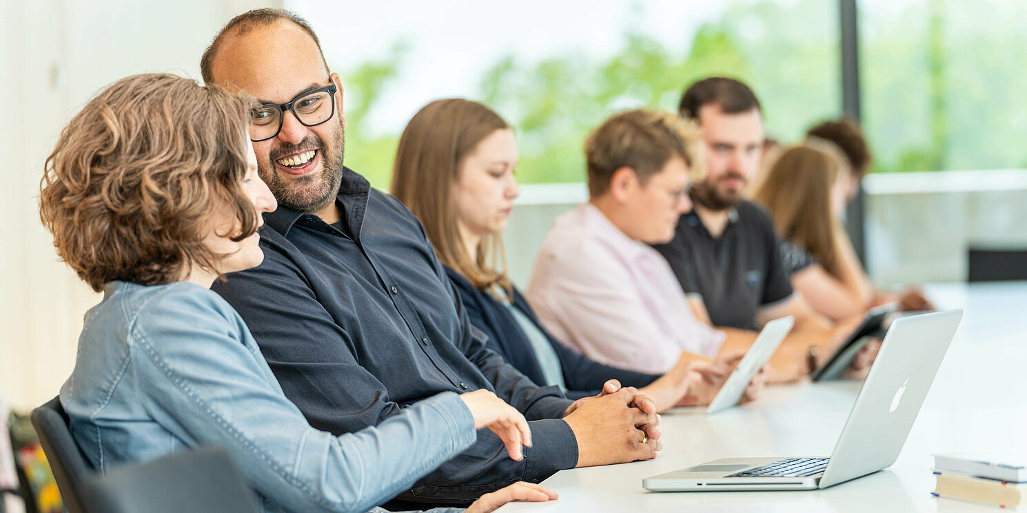 Mehrere Personen sitzen in einer Reihe an Tischen