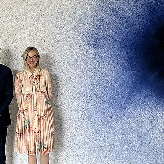 Ein Mann und eine Frau stehen vor einer Wand mit einem Kunstwerk.