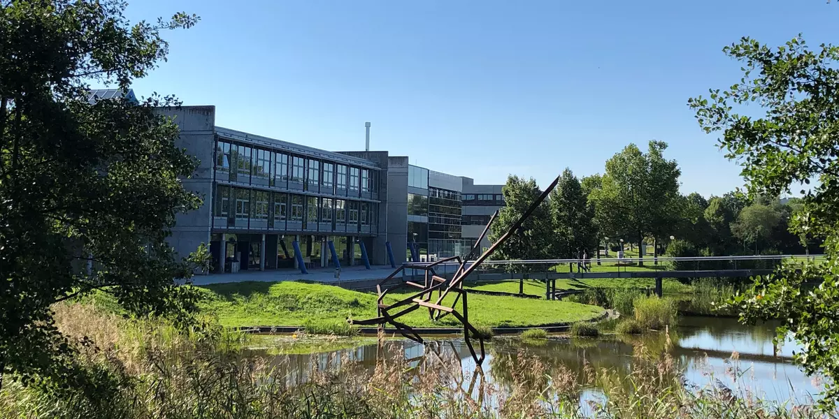 Campusansicht, im Vordergrund der See, im Hintergrund die Fakultät Maschinenbau, darüber blauer Himmel.