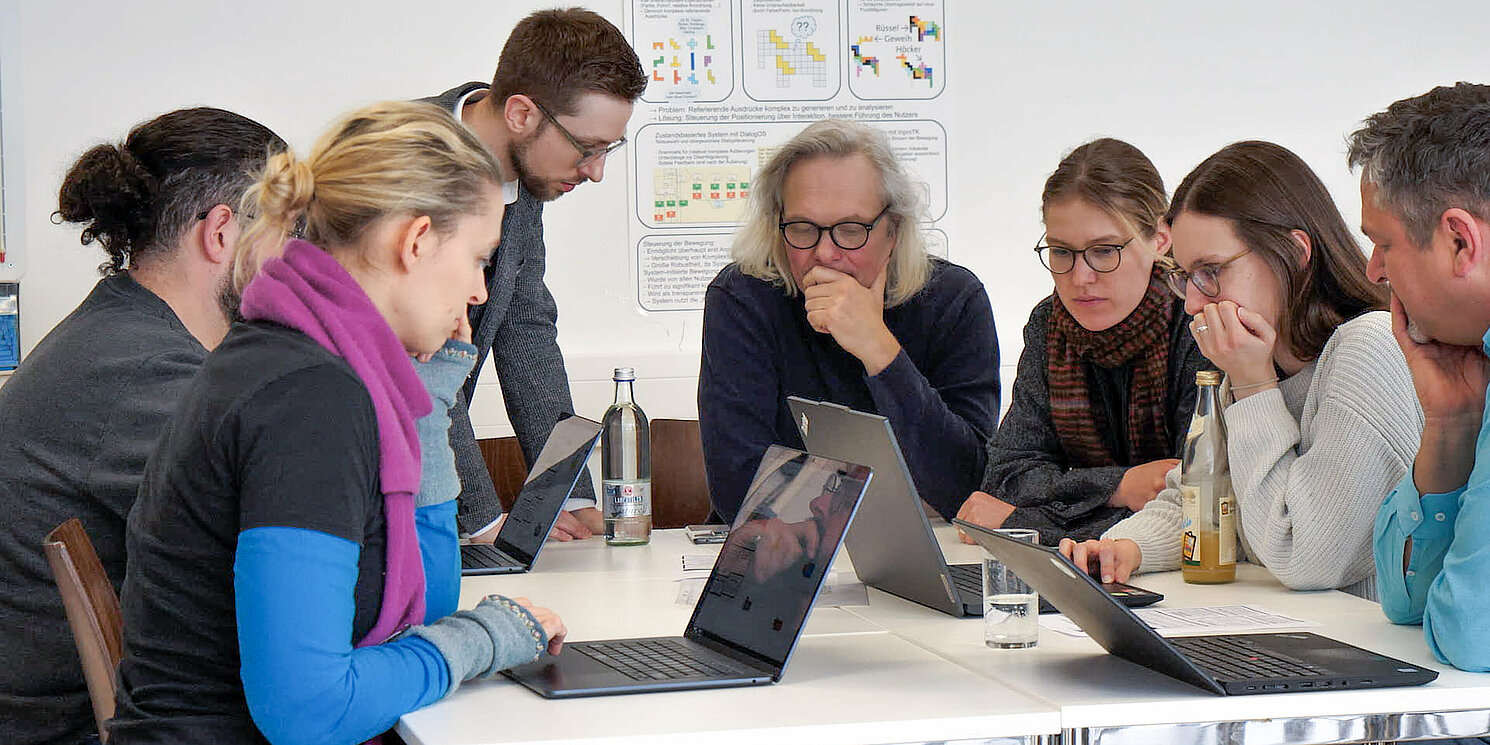 Mehrere Menschen arbeiten an einem Tisch an Laptops.